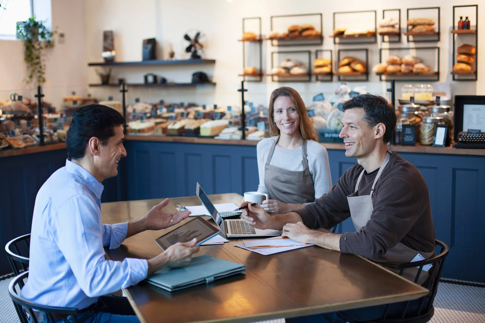 un homme qui conseille un couple de gérants d'une boulangerie autour d'une table